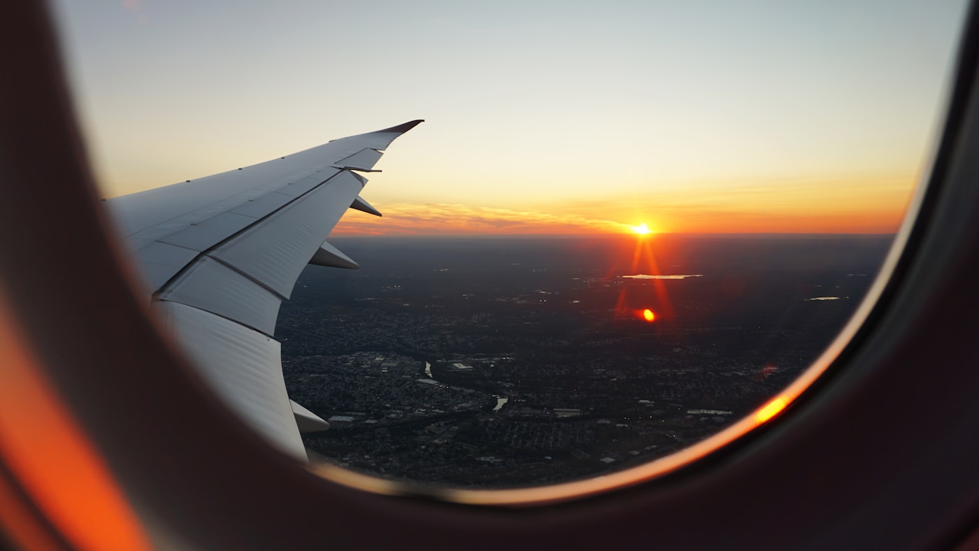 View from an aeroplane window of the wing and a city below at sunset
