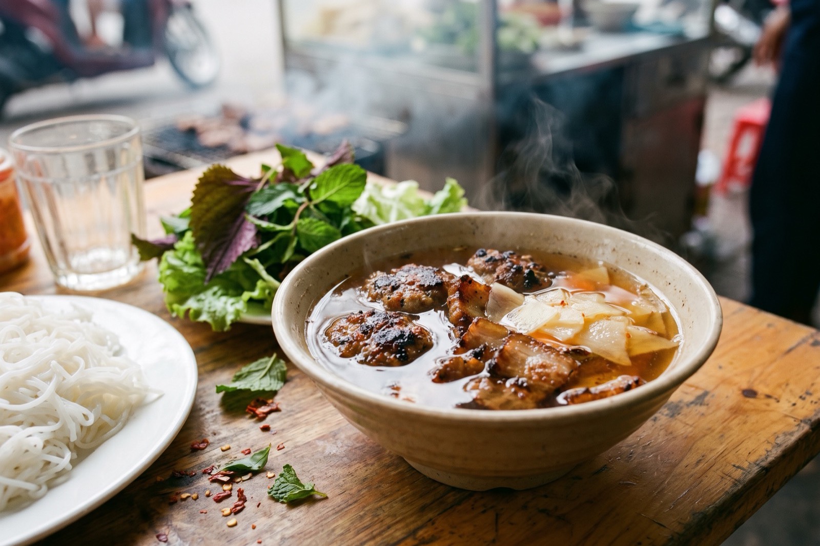 Bowl of bun cha with grilled pork patties in fish sauce broth, served with rice noodles and fresh herbs.